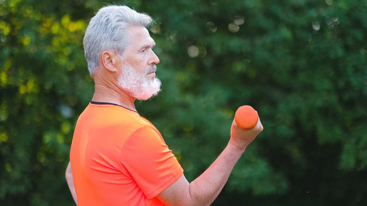 Older man performing resistance training with a dumbbell outdoors